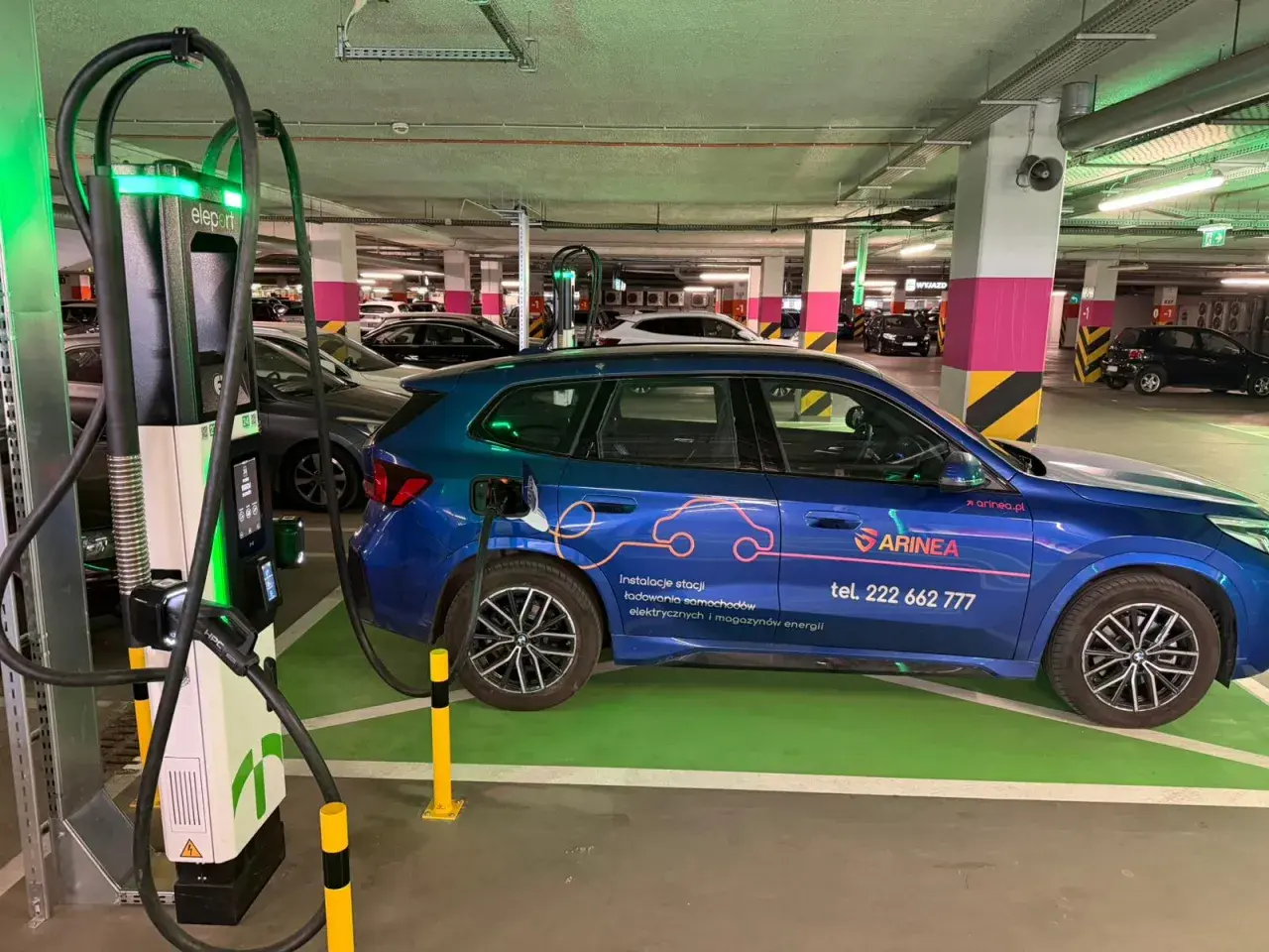 Niebieski samochód elektryczny ładuje się przy stacji typu wallbox w podziemnym parkingu. To przyszłość transportu!