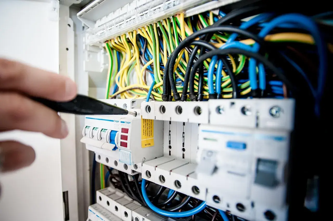 Ręka z narzędziem przy skrzynce z bezpiecznikami i przewodami. Kluczowe dla planowania elektryki w domu.