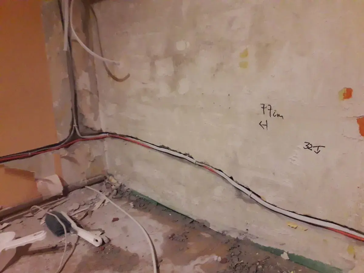 Skrętka obok kabla elektrycznego biegnie wzdłuż ściany. Na tynku widoczne oznaczenia "77cm" i "32J".