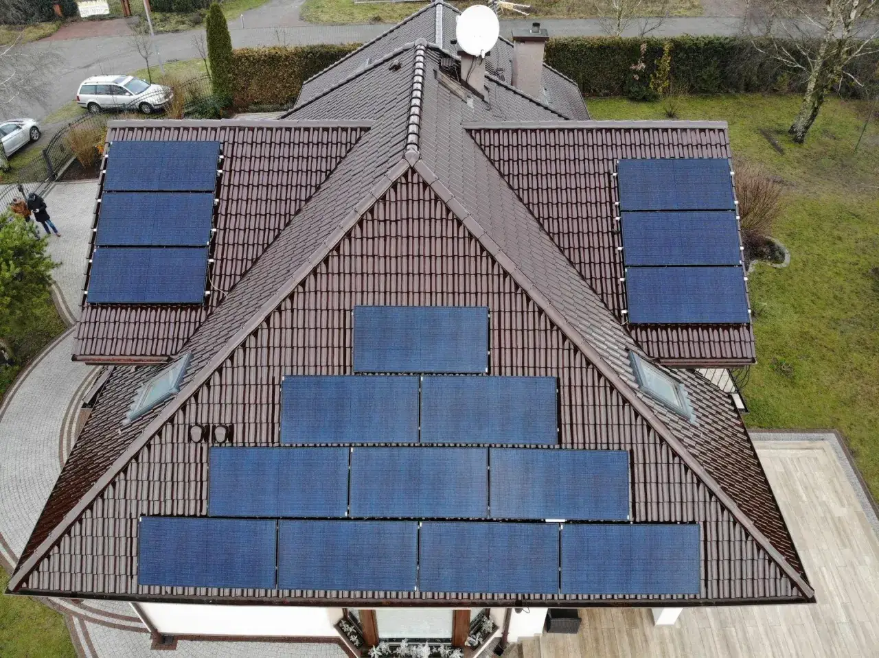Dach domu pokryty brązową dachówką, z zamontowaną instalacją fotowoltaika moc. Panele słoneczne rozmieszczone na kilku połaciach dachu.