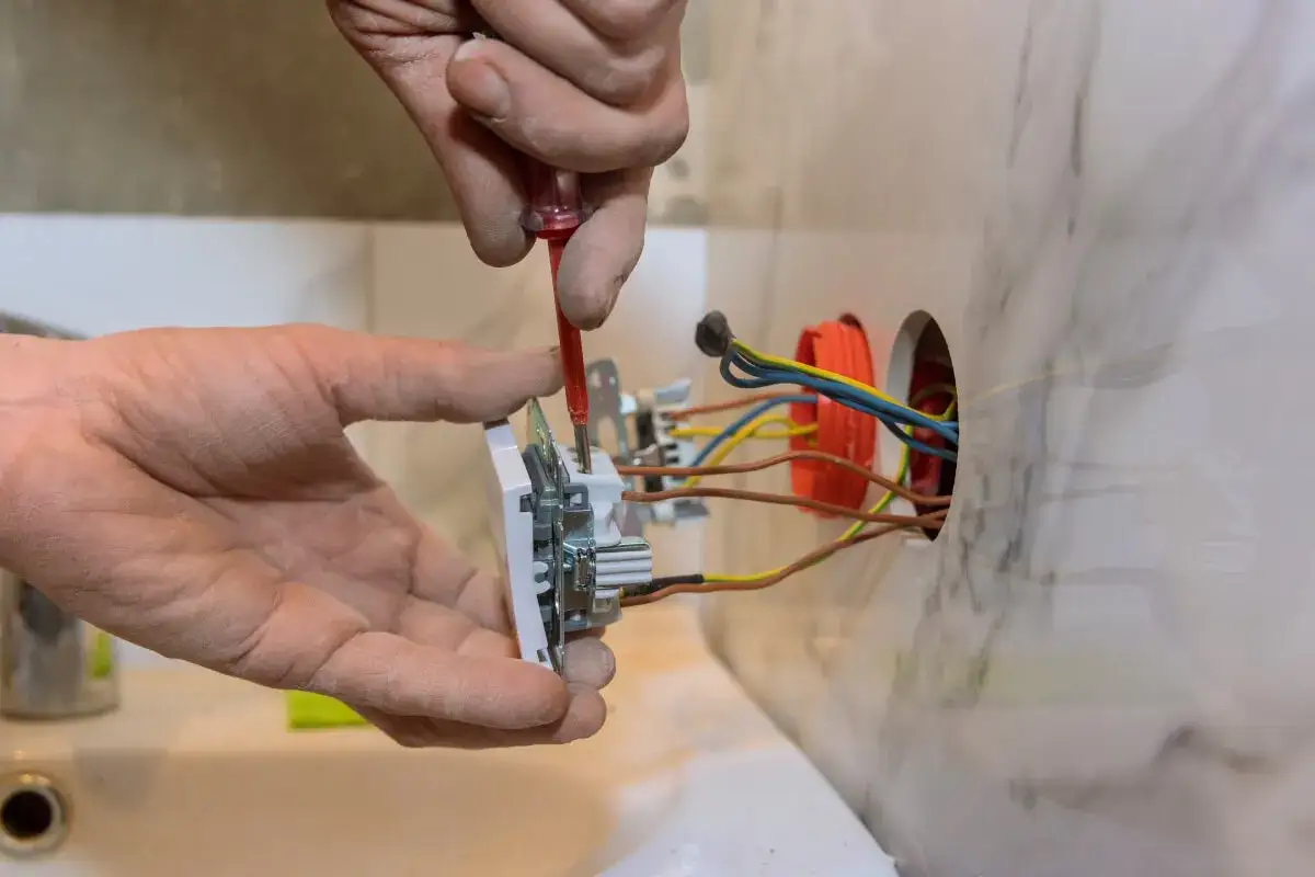 Ręce majsterkowicza przykręcają nowe gniazdko. Widać przewody elektryczne wychodzące ze ściany.