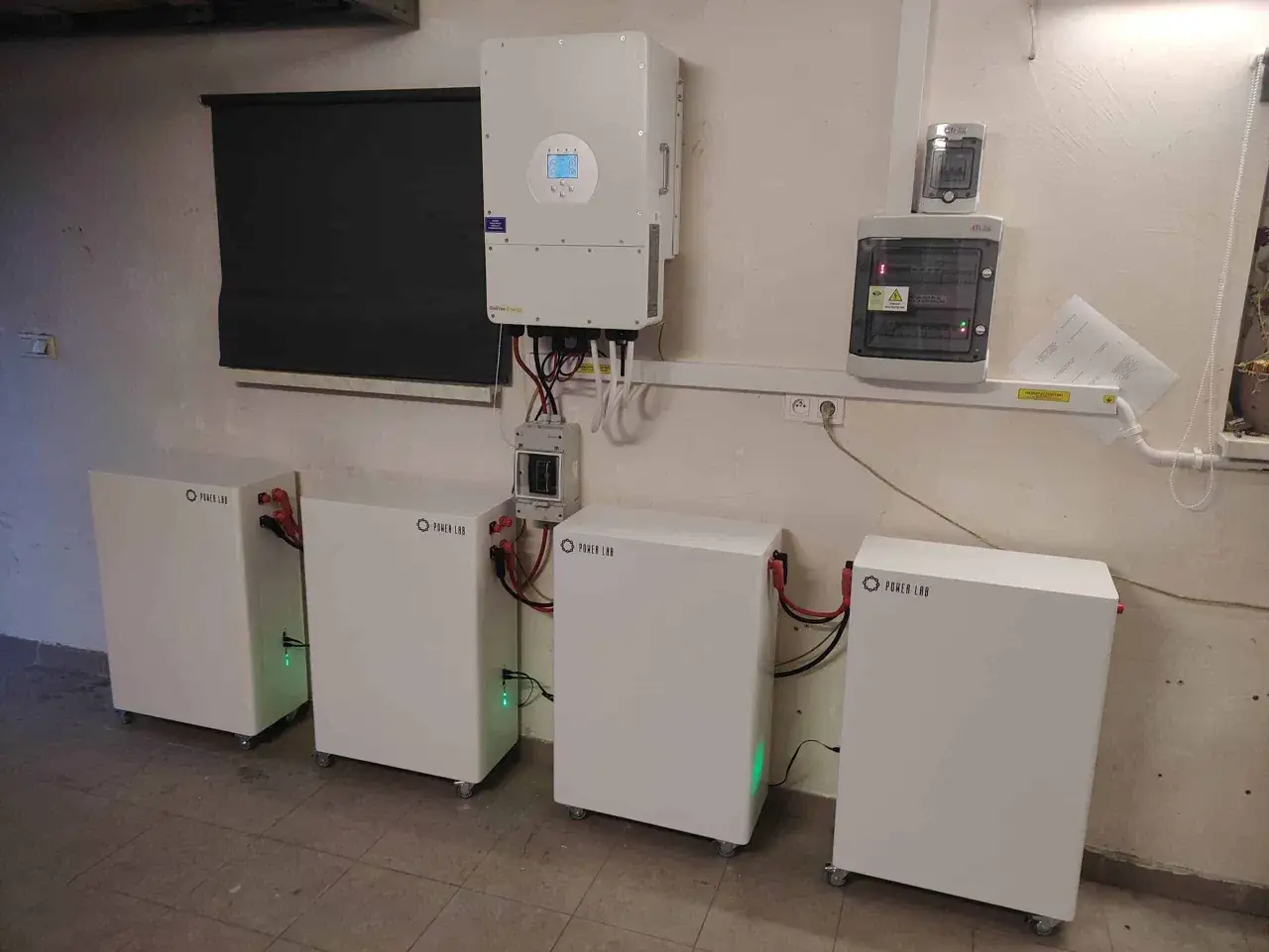 System off grid: cztery baterie Power Lab, falownik i skrzynka rozdzielcza. Zielone światła wskazują gotowość.