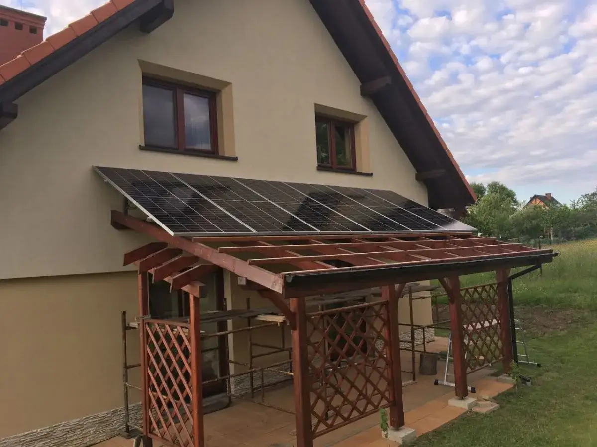 Panele fotowoltaiczne na drewnianej konstrukcji nad tarasem, tworzące zadaszenie. Ekologiczne rozwiązanie dla domu.
