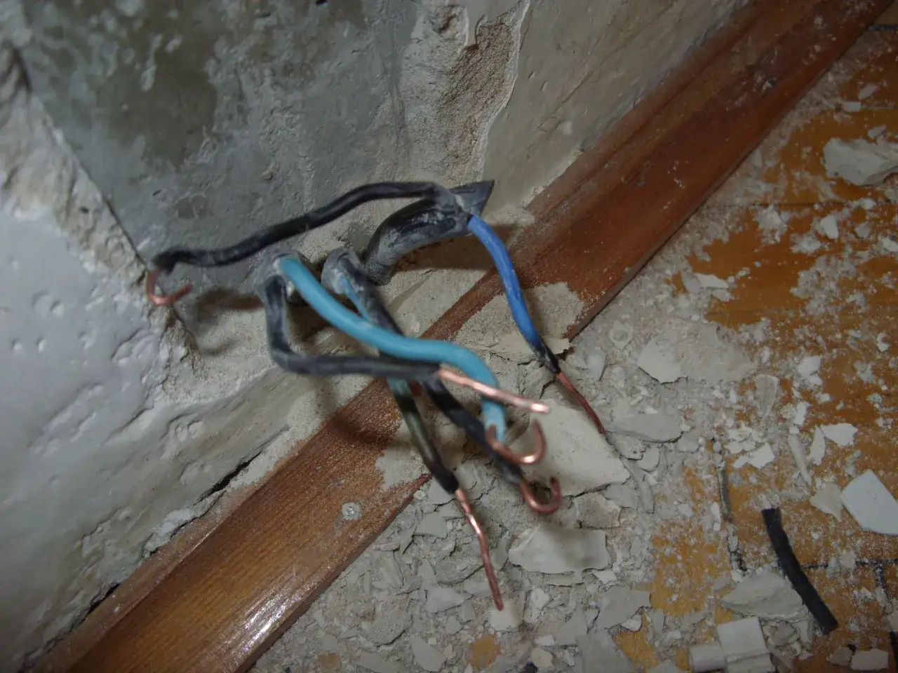 Luźne przewody elektryczne, w tym niebieski przewód neutralny, wystają z betonowej ściany. Widać odsłonięte miedziane końcówki, co może oznaczać małe napięcie na przewodzie neutralnym.