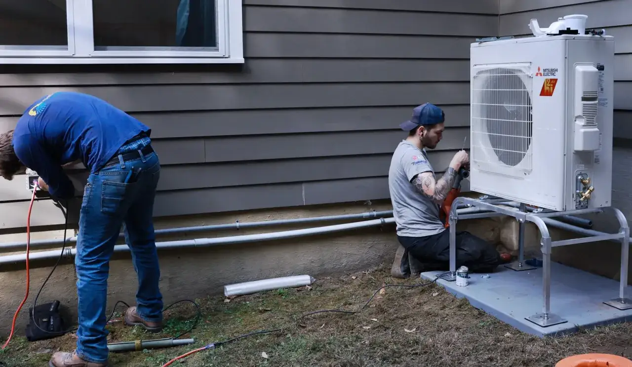 Instalacja pompy ciepła 12kw na ile metrów domu? Dwóch techników pracuje przy jednostce zewnętrznej, podłączając przewody i mocując ją.