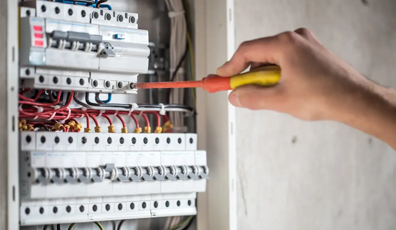 Elektryk naprawia instalację, gdzie różnicówka wybija pod obciążeniem. Widać bezpieczniki i przewody.