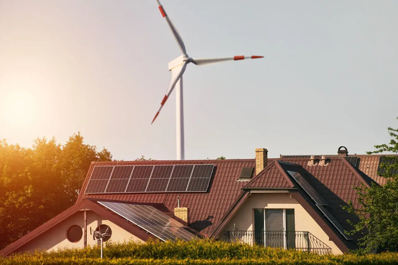 Dom z panelami słonecznymi na dachu i wiatrak w tle, symbolizujące ekologiczne źródła energii.