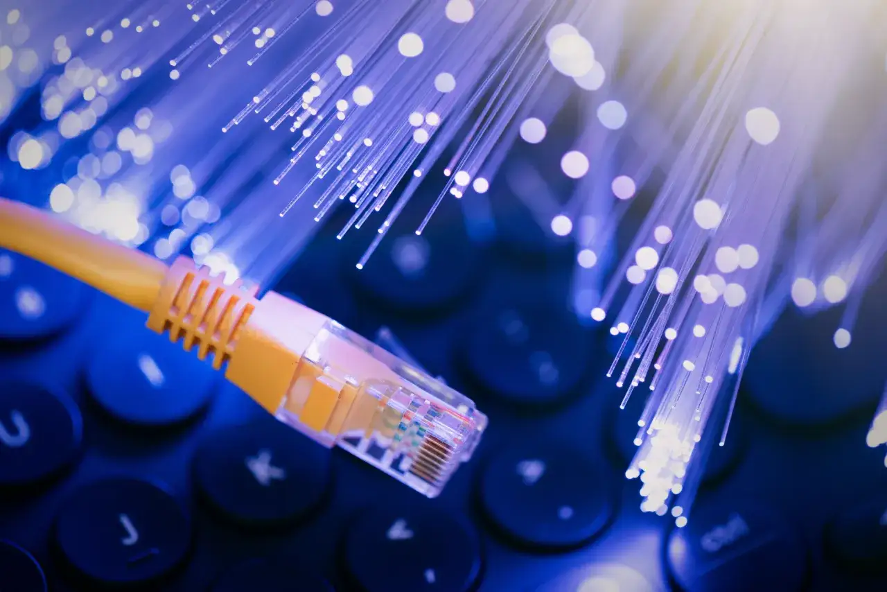 Ż&oacute;łty kabel sieciowy na klawiaturze, otoczony przez świecące światłowody symbolizujące szybki internet po kablu koncentrycznym.