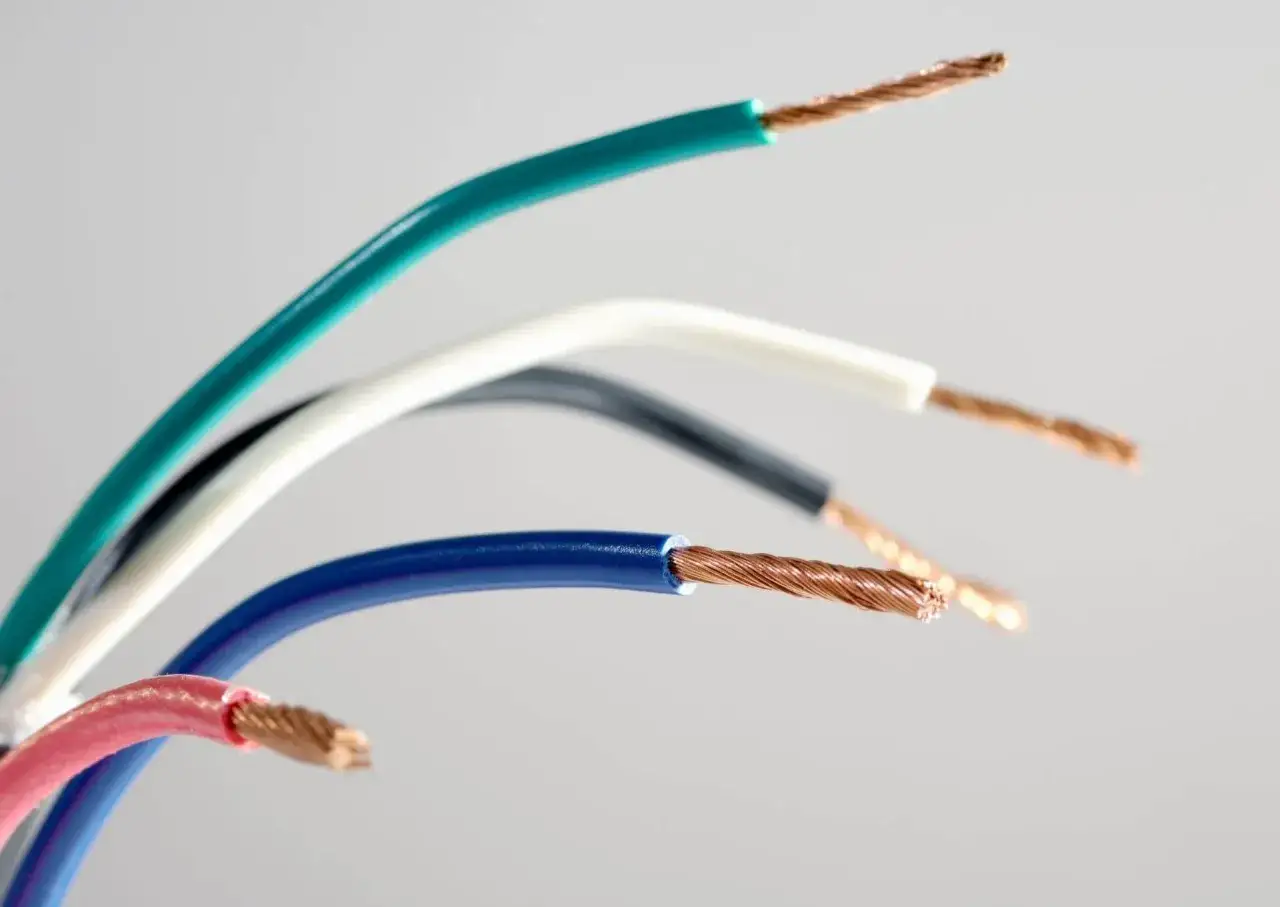 Kolorowy przewód elektryczny, z odsłoniętymi miedzianymi żyłami, tworzy tęczowy łuk na jasnym tle.