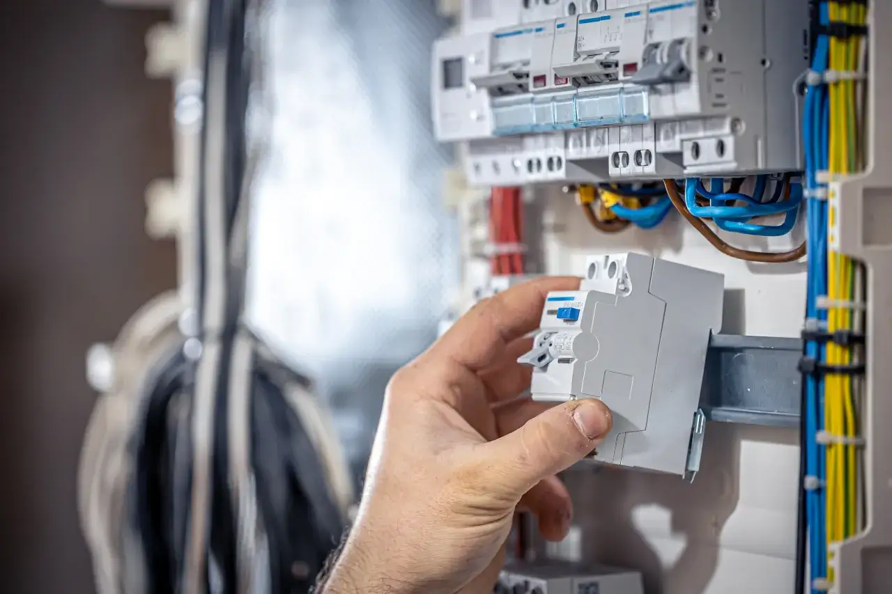 Dłoń montuje bezpiecznik w skrzynce elektrycznej. Gdy wywaliło korki jak włączyć, trzeba sprawdzić instalację.