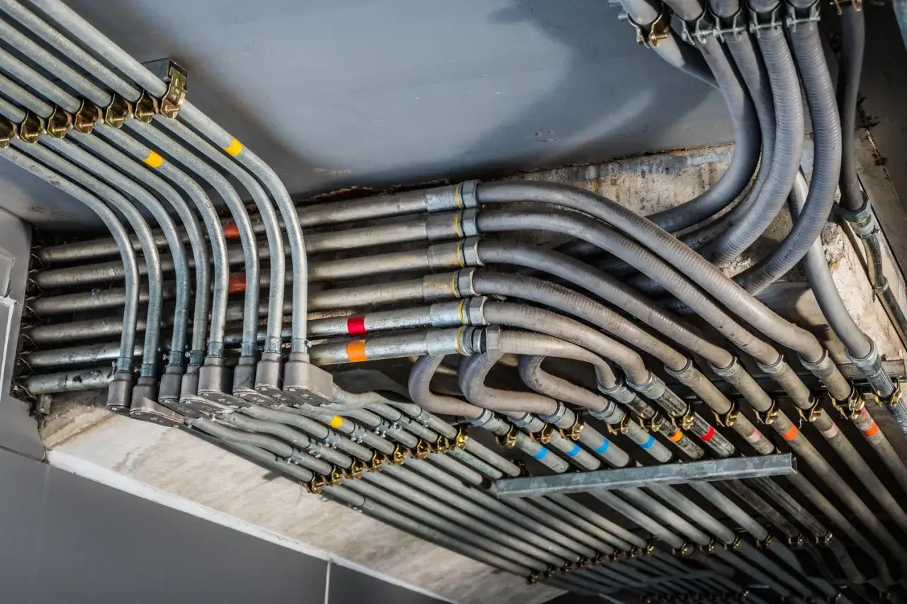 Zabezpieczenie przewodów elektrycznych w postaci wielu metalowych i plastikowych rur, biegnących równolegle i zakrzywionych, z kolorowymi oznaczeniami.