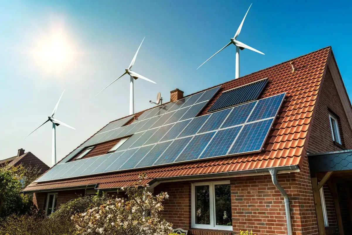 Dom z panelami słonecznymi i turbinami wiatrowymi, symbolizującymi czystą energię z wiatru i słońca.