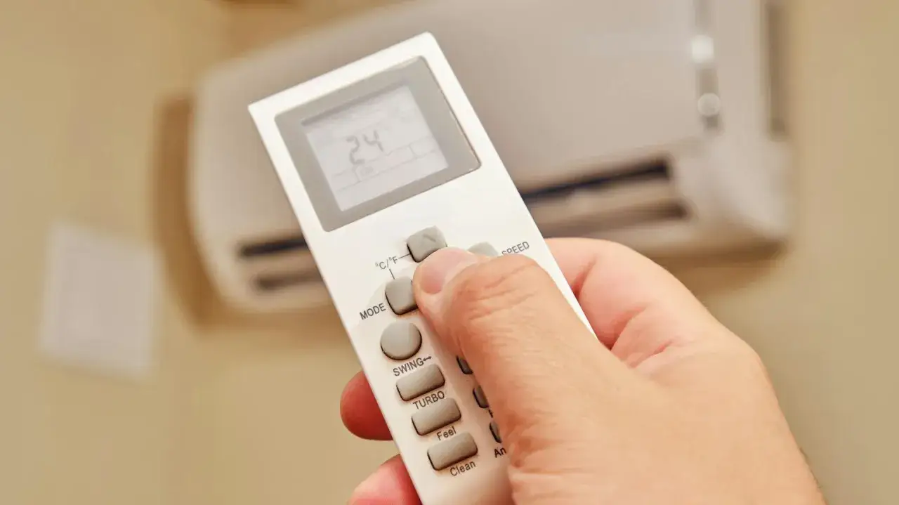 Dłoń steruje pilotem klimatyzacji, ustawiając temperaturę 24°C. Ogrzewanie klimatyzacją zapewnia komfort.